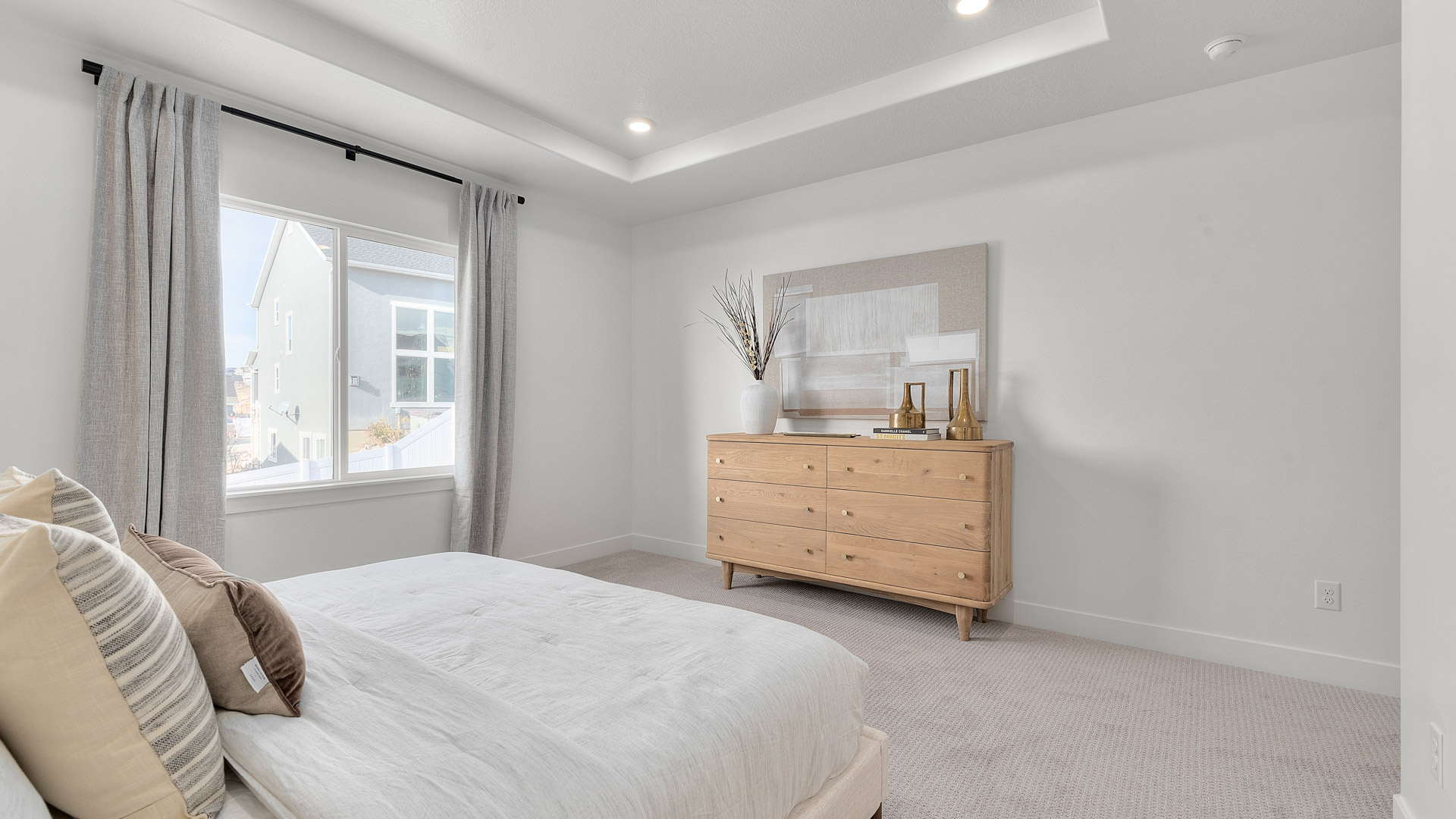 Spacious primary bedroom with tray ceilings and large window.