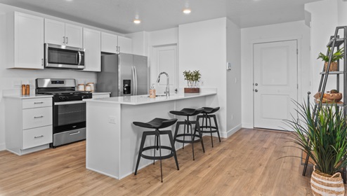Kitchen space with peninsula featuring barstools, sink, kitchen cabinets, and appliances.