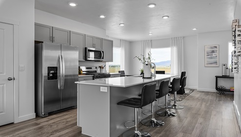 Open kitchen with a large island and sink, plenty of counterspace, light grey shaker cabinets and stainless steel appliances.