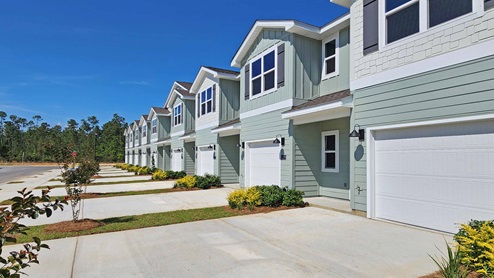 Two-story townhomes with misty green siding with shake accents and one car garage.