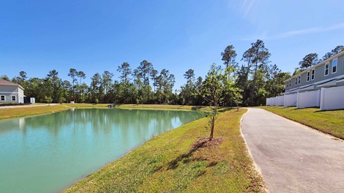 Walking trail view around community pond with townhomes in the distance.