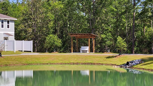 Pond view with a pergola and townhomes in the background.