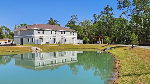 Pond view with a pergola and townhomes in the background.
