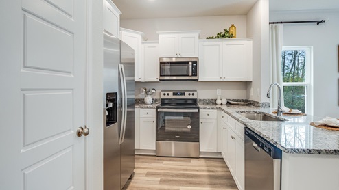 Pantry and kitchen area with white shaker-style cabinetry and stainless-steel applicances.