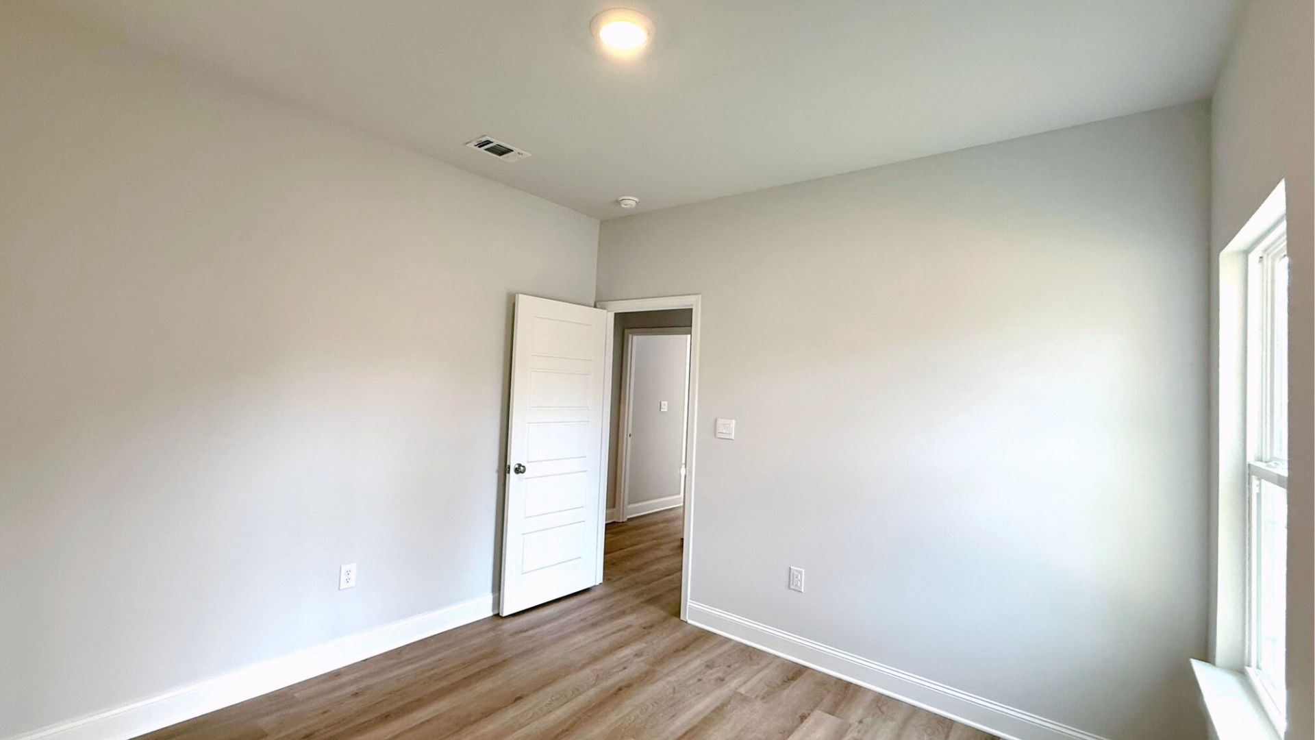 Bedroom with brown flooring and a window.