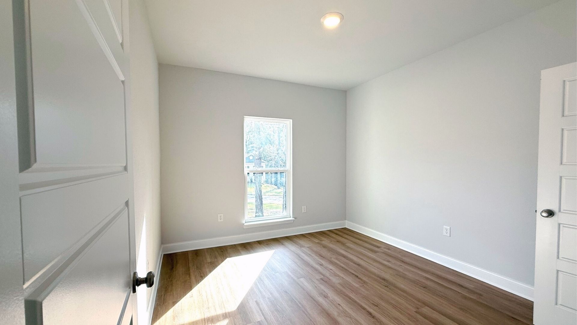 Bedroom with brown flooring and a window.