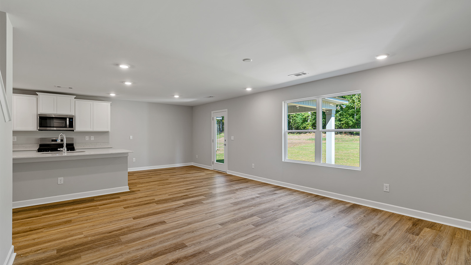 Open concept living room with LVP flooring and seamless flow to the kitchen and dining area.