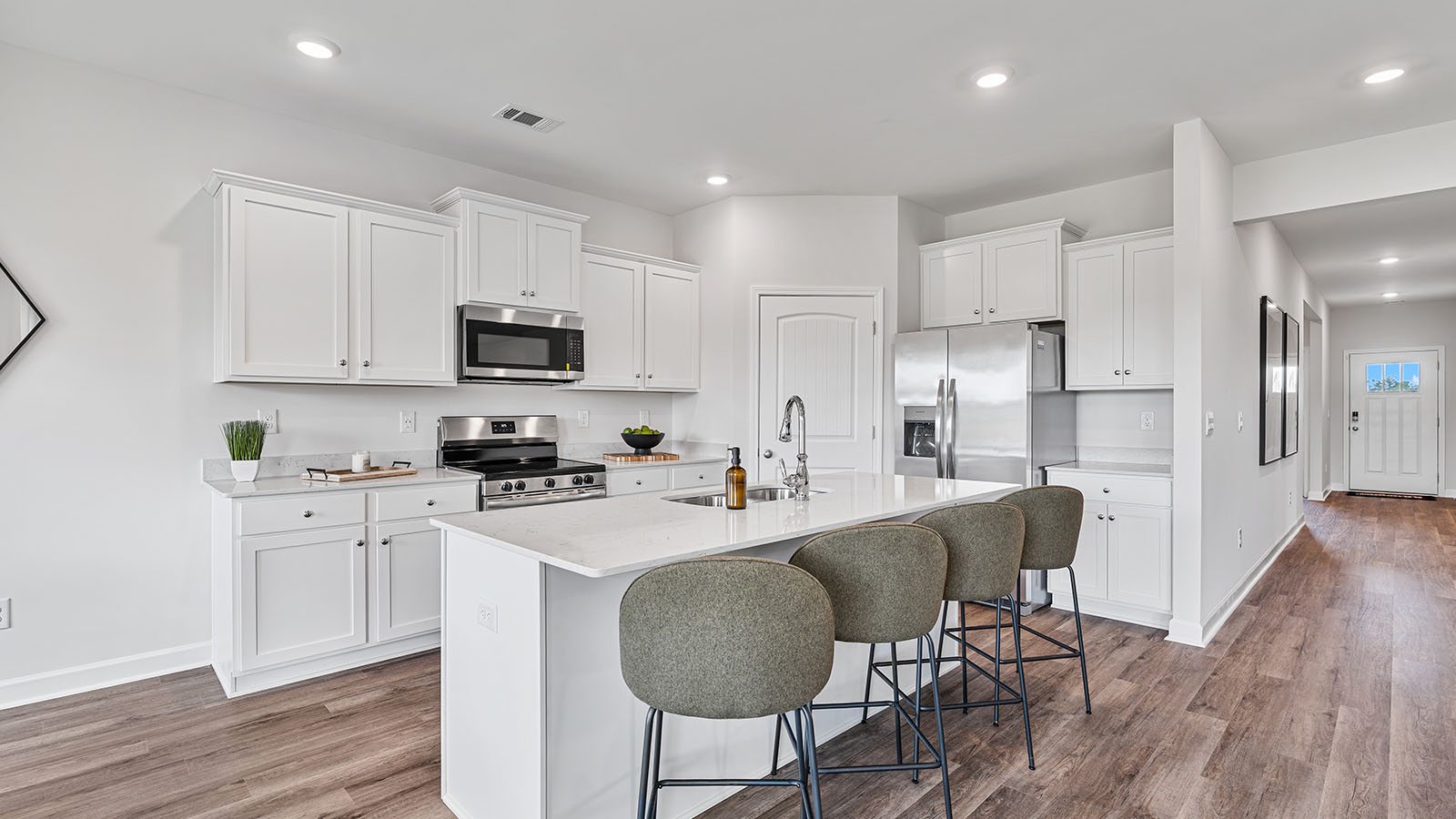 Open kitchen with stainless steel appliances and clean, quartz finished workspace.