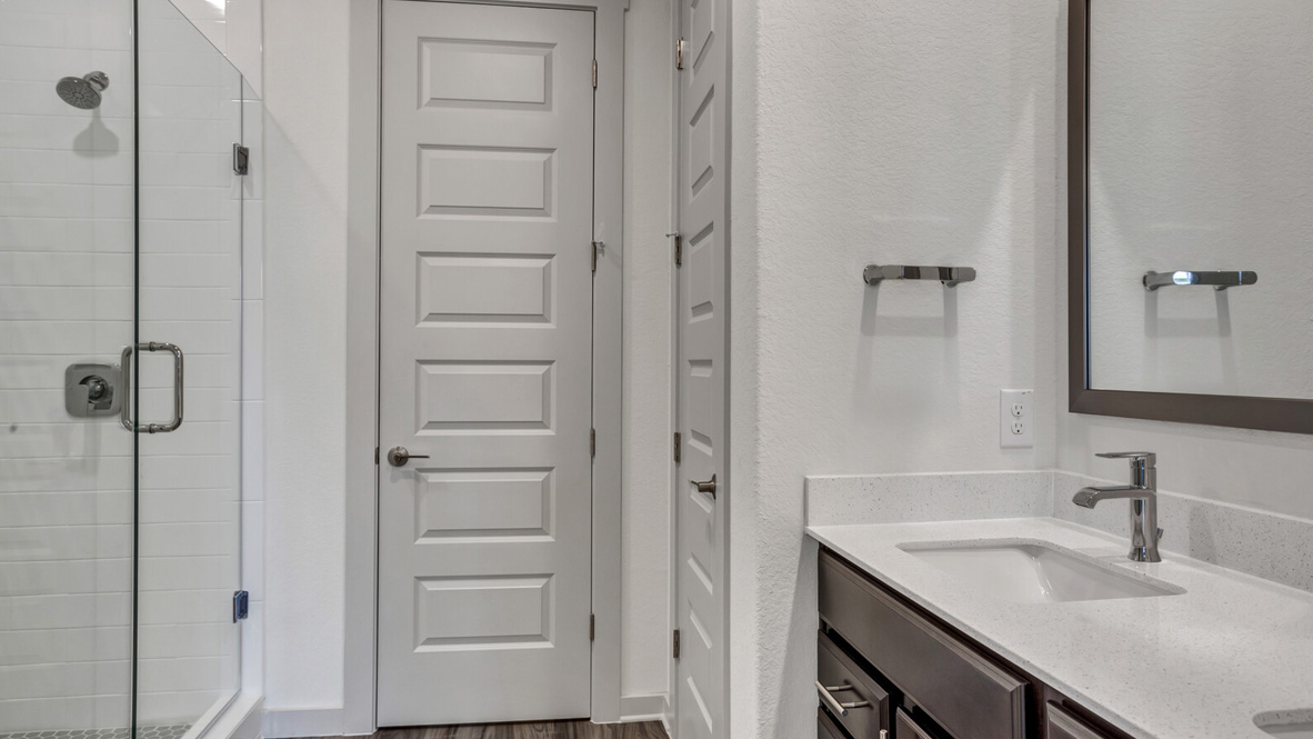 Bathroom with dual sinks, a walk in shower, and doors leading to closet and toilet.