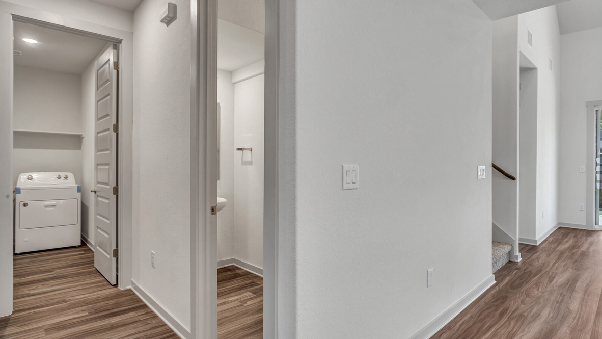 Hallway with brown flooring and white walls leading to laundry room and a bathroom.