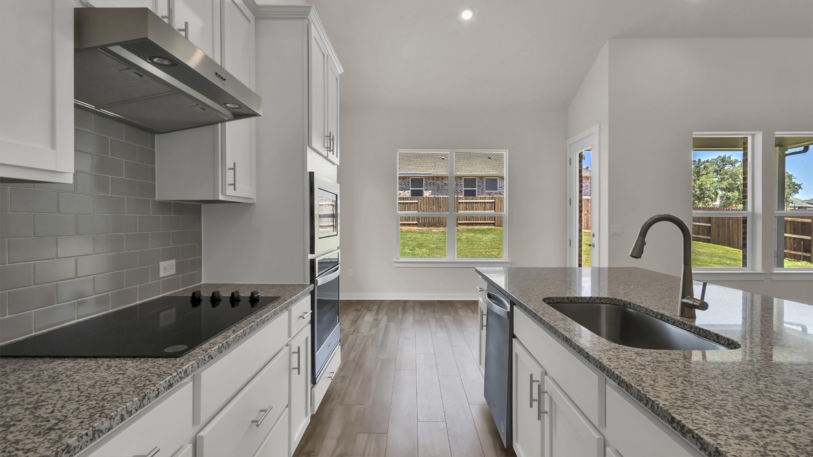 New appliances and central kitchen island with seating anchor the kitchen, next to dining, great room, backyard access