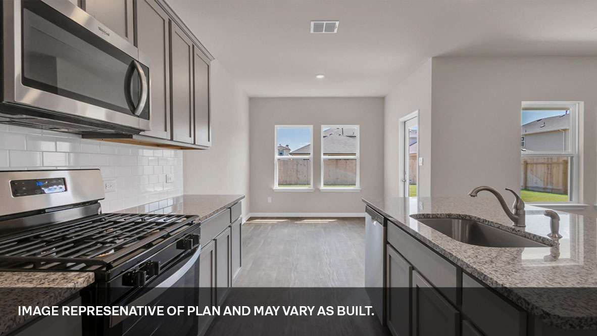 Side view of the kitchen area with tan/gray granite countertops, large island, light gray cabinets, and stainless steel appliances with pantry in the corner.