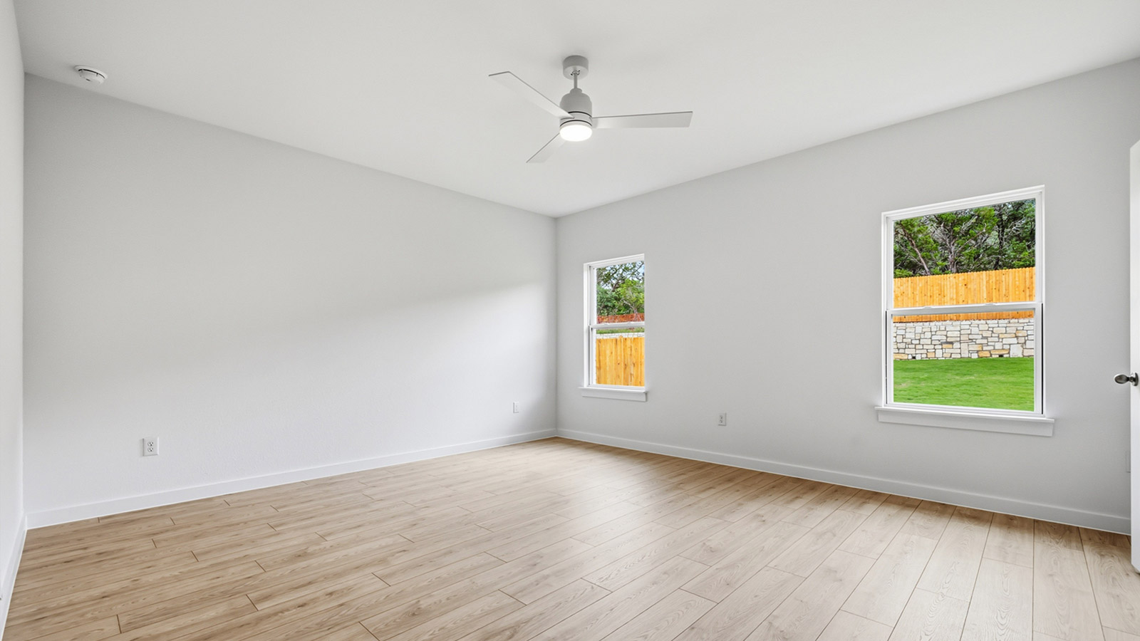 Spacious primary bedroom with a ceiling fan and two windows.