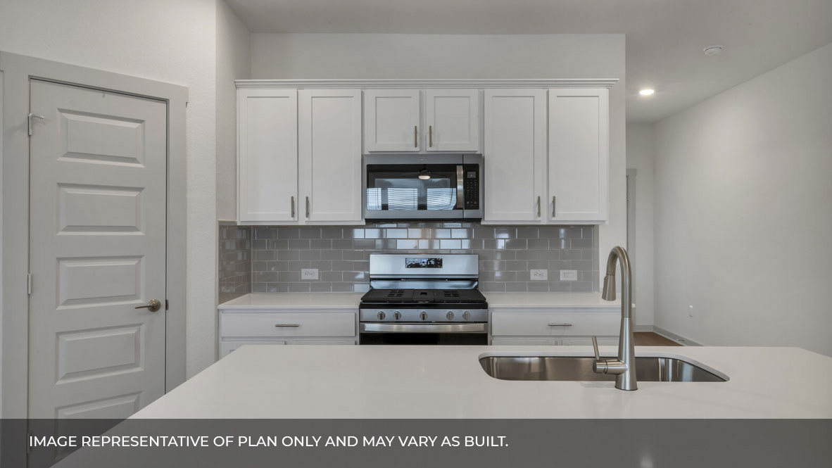 Front view of the kitchen area with white granite countertops, large island, white cabinets, light gray backsplash, and stainless steel appliances with pantry in the corner.