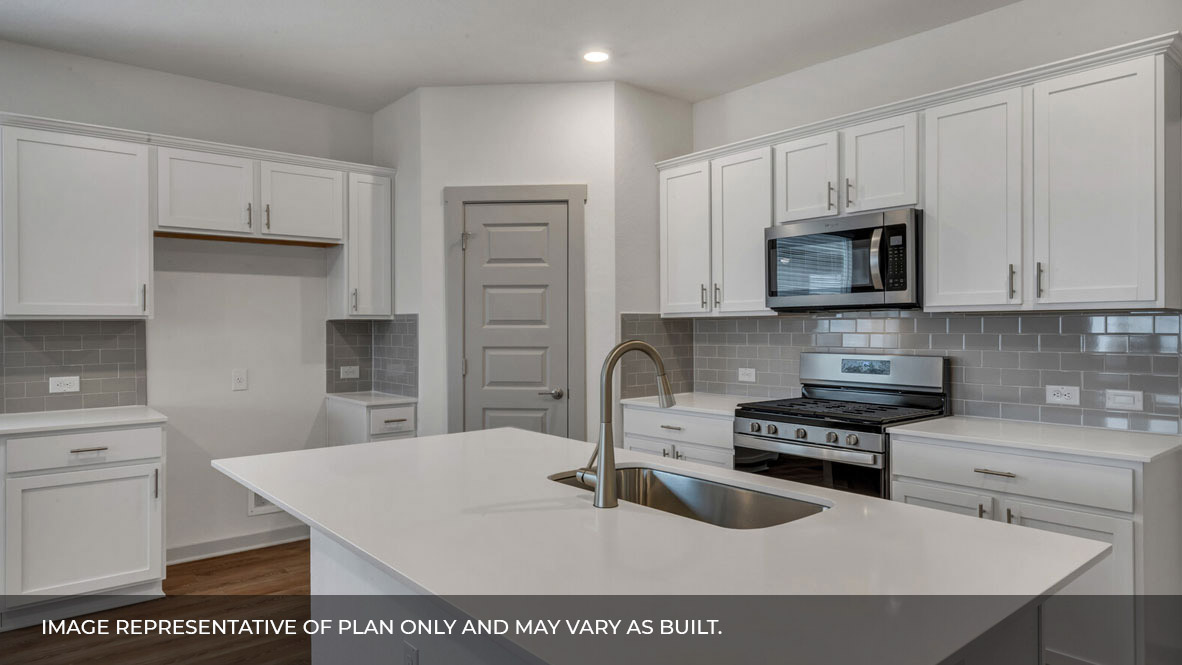 Kitchen area with white granite countertops, large island, white cabinets, light gray backsplash, and stainless steel appliances with pantry in the corner.