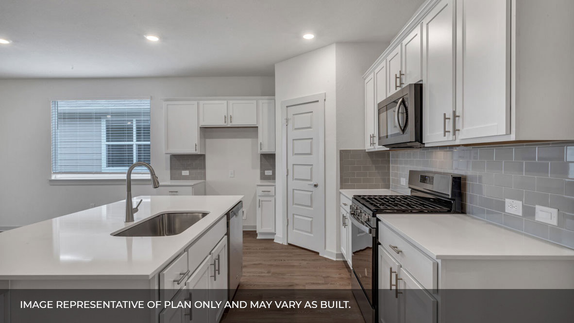Side view of the kitchen area with white granite countertops, large island, white cabinets, light gray backsplash, and stainless steel appliances with pantry in the corner.