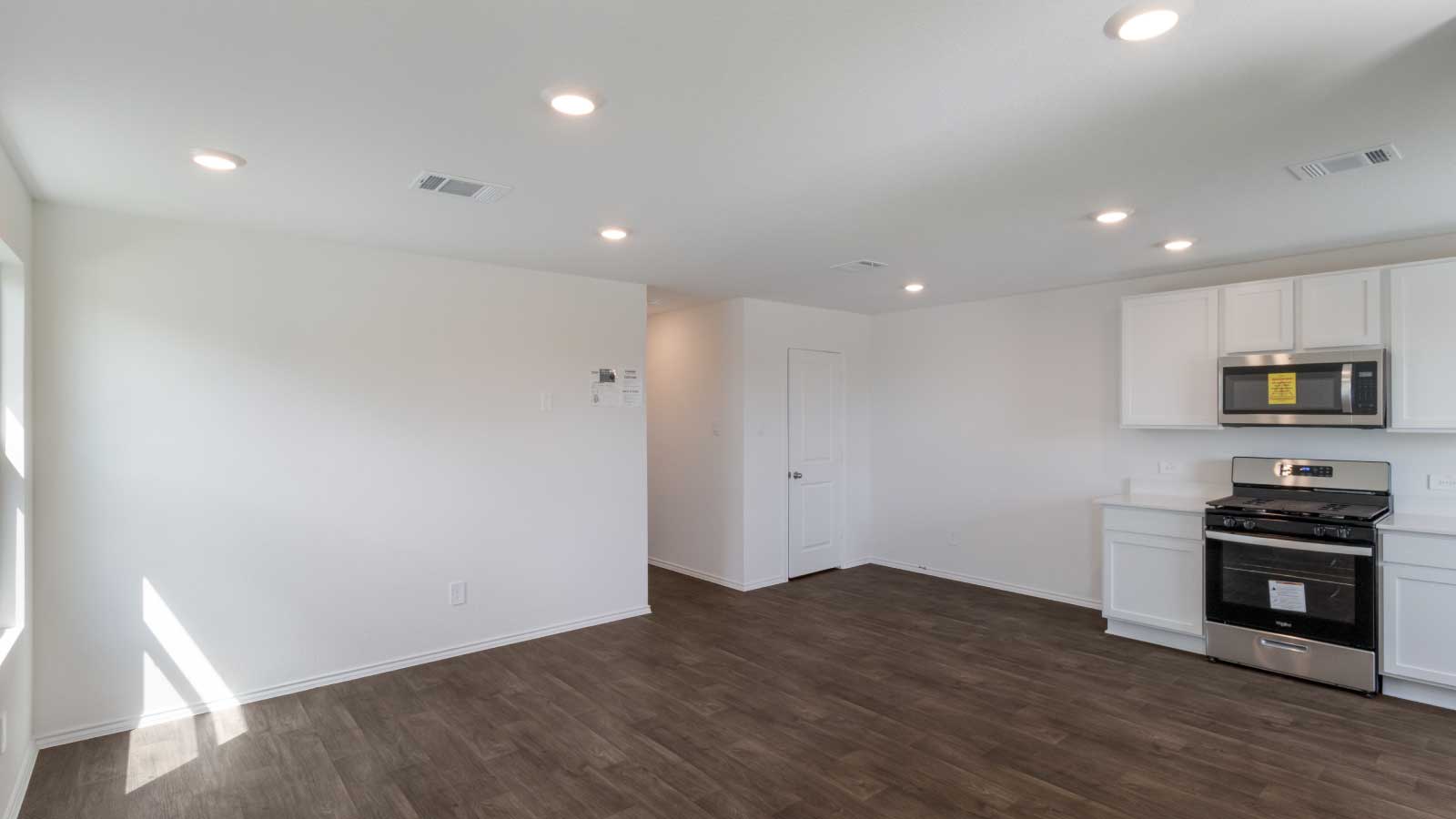 Living room with dark brown flooring and white walls connected to the kitchen.