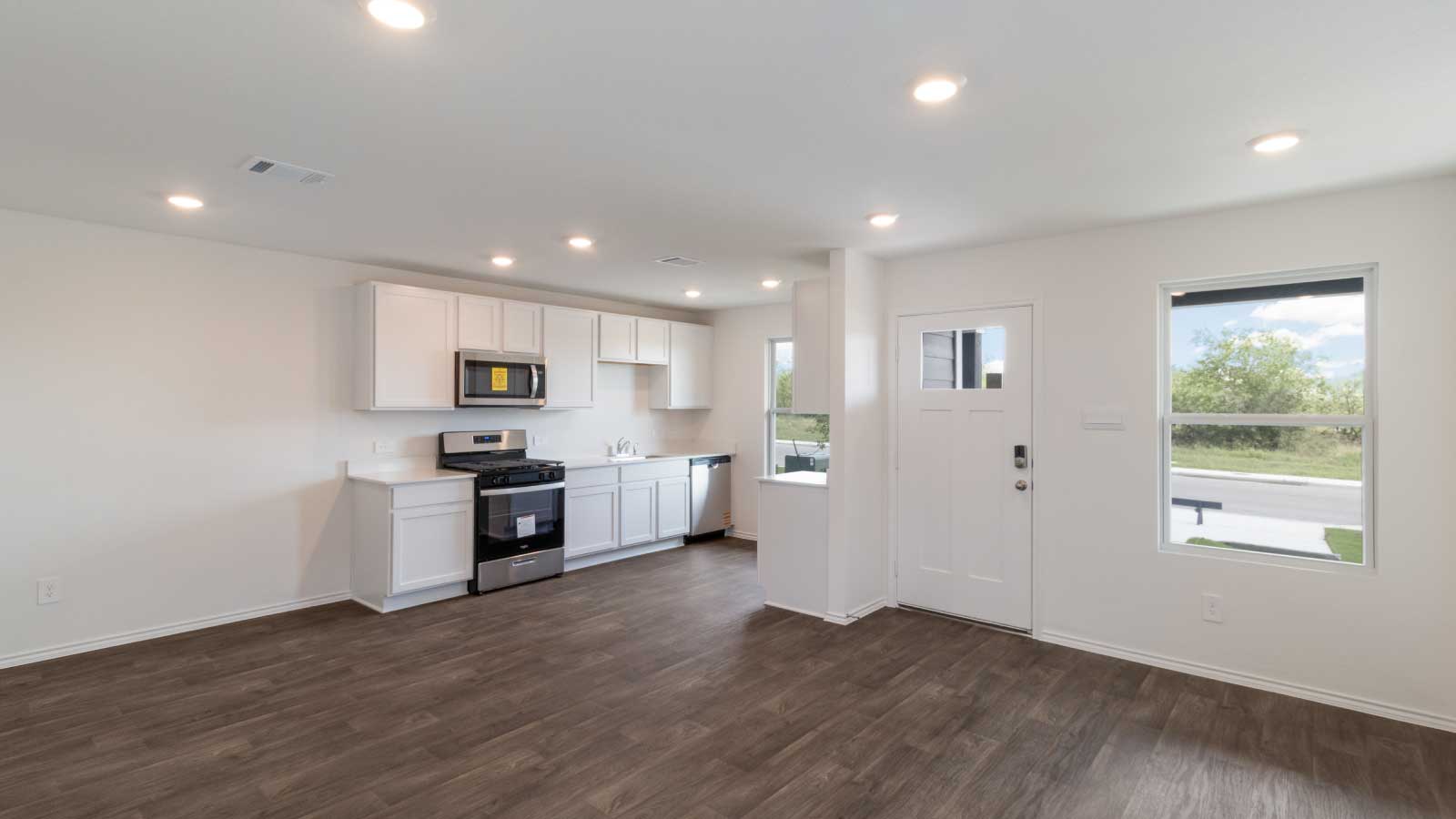 Living room with dark brown flooring and white walls connected to the kitchen.