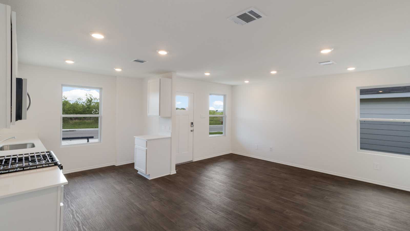 Living room with dark brown flooring and white walls connected to the kitchen.