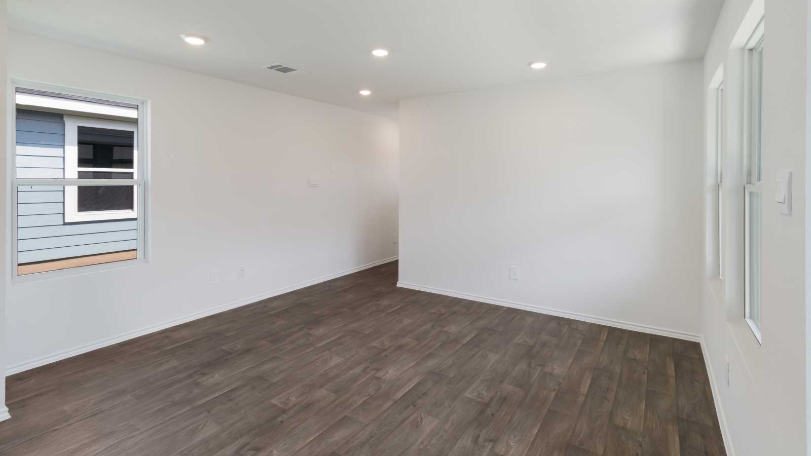 Living room area with dark brown flooring, white walls, and a large window.
