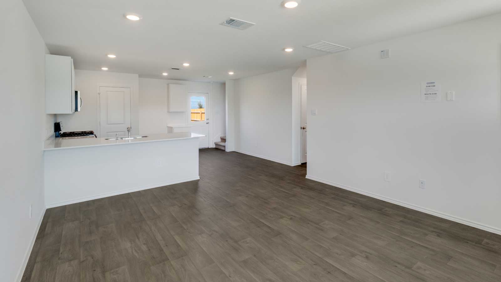 Living area with brown flooring and white walls connecting to the kitchen.
