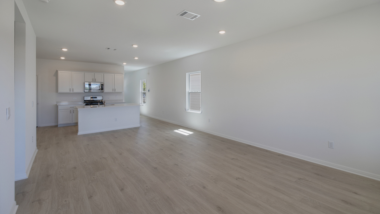 Living area connecting to kitchen with brown flooring and white walls.