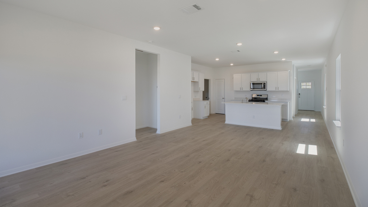Living area connecting to kitchen with brown flooring and white walls.