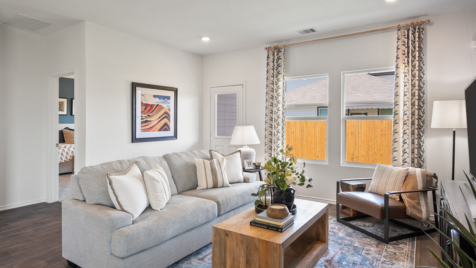 Bright living room with two windows and furnished with a gray sofa, an armchair, and a wooden coffee table