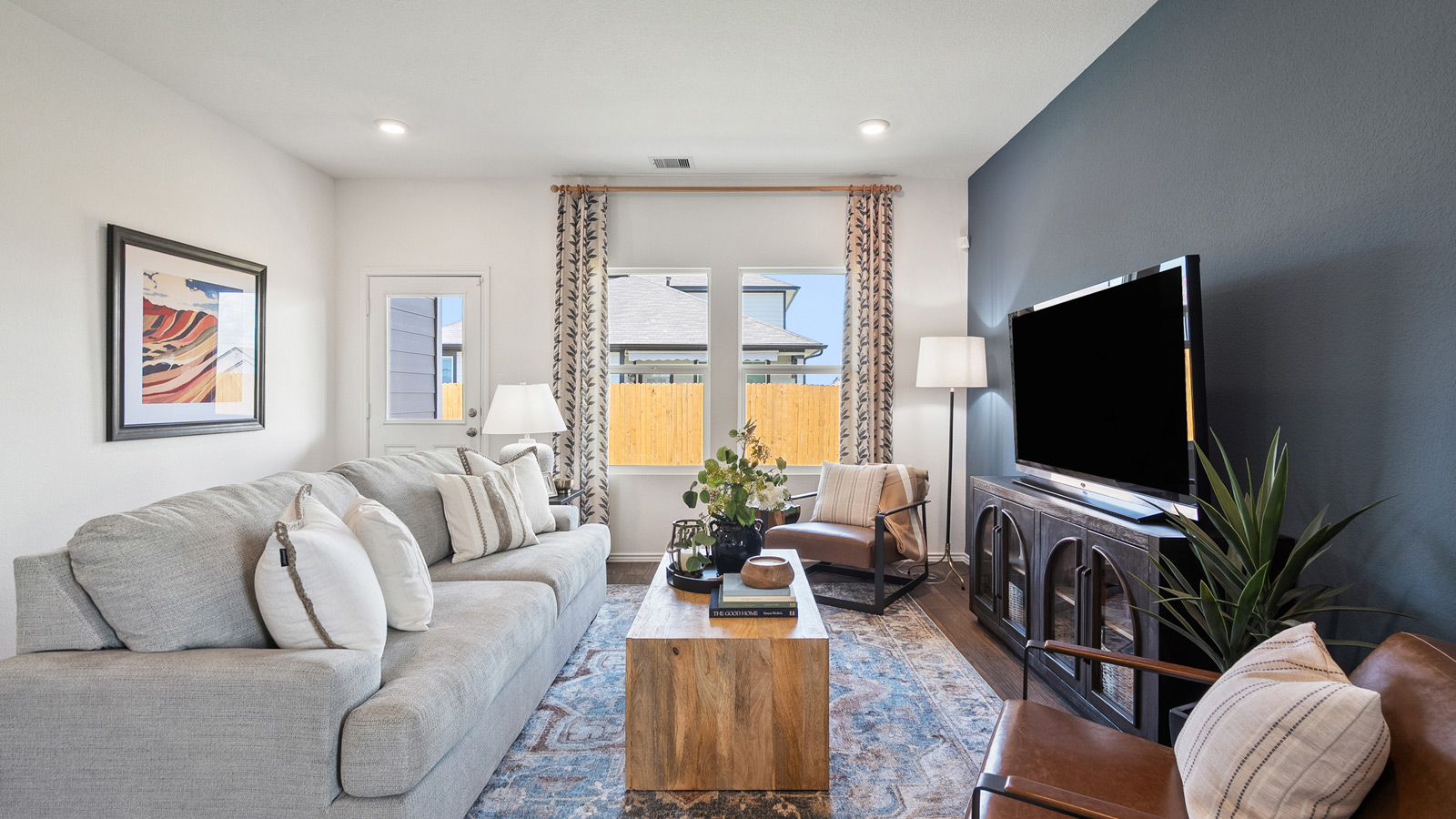 Side view of a bright living room with two windows and furnished with a gray sofa, a wooden coffee table, a TV, and TV stand