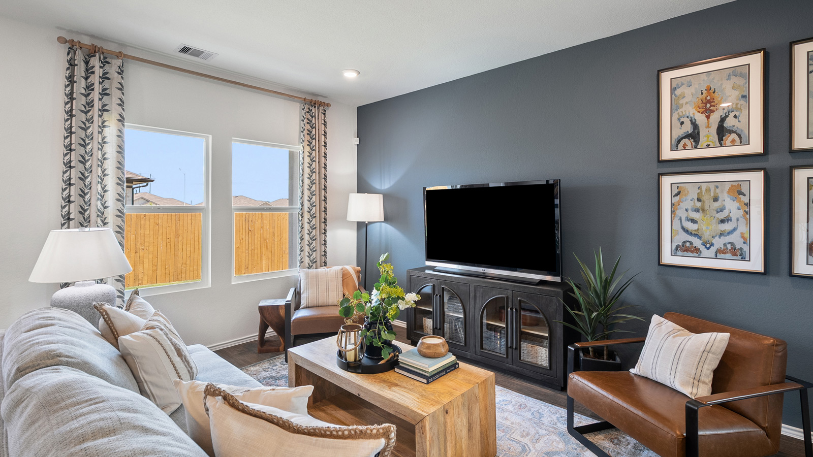 Bright living room with two windows and furnished with a gray sofa, a wooden coffee table, two armchairs, a lamp, a TV, and a TV stand