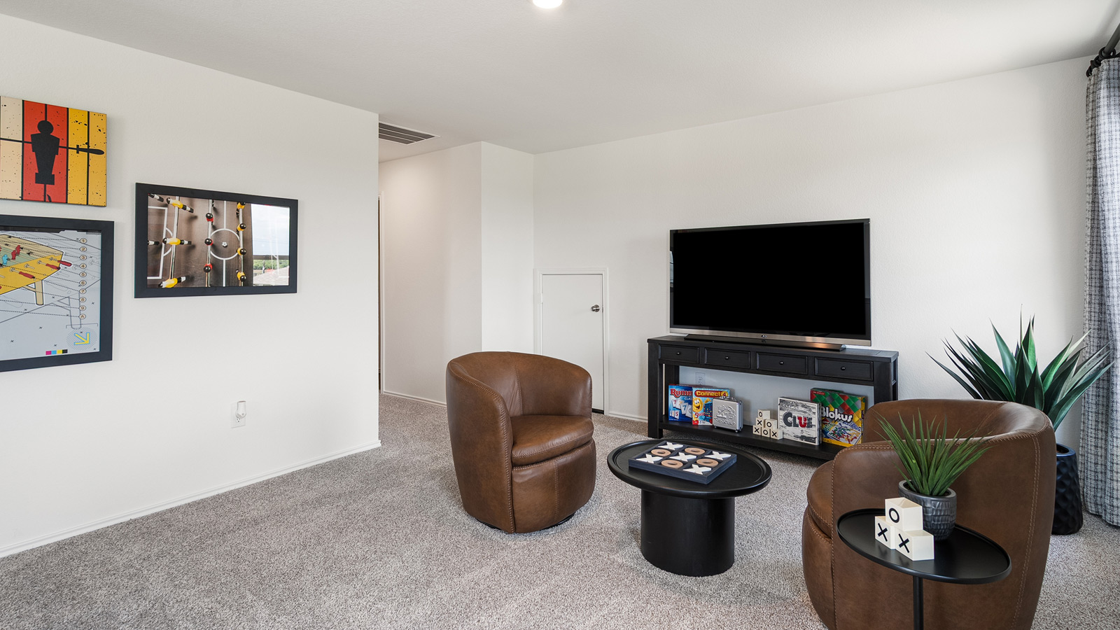 Gameroom with overhead lighting and furnished with two chairs, a small round table, a TV, and TV stand.