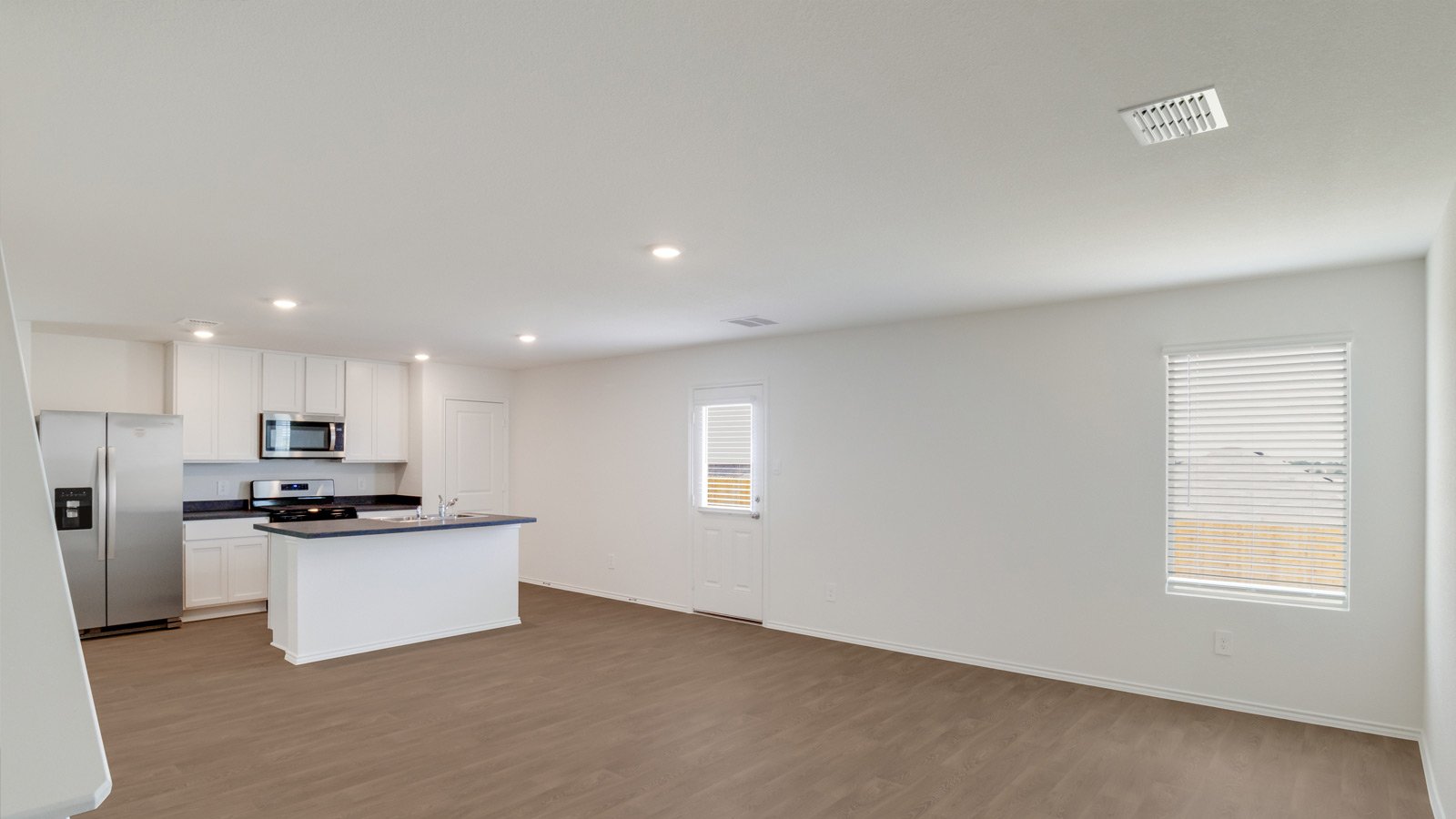 Main living area with clean flooring and natural light connecting to kitchen.
