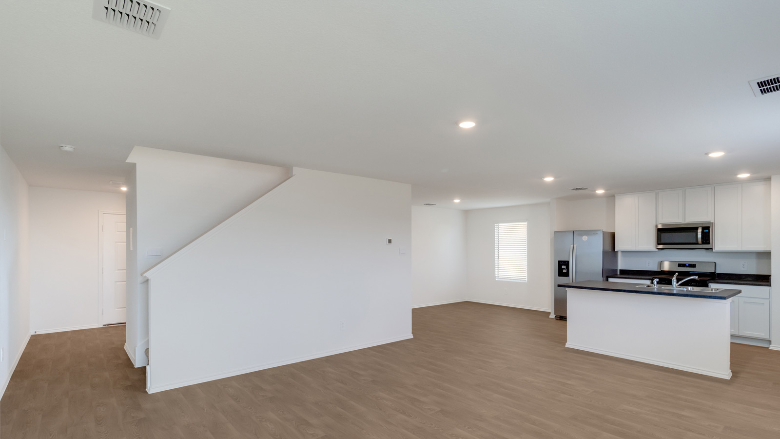 Main living area with clean flooring and natural light connecting to kitchen and a staircase.
