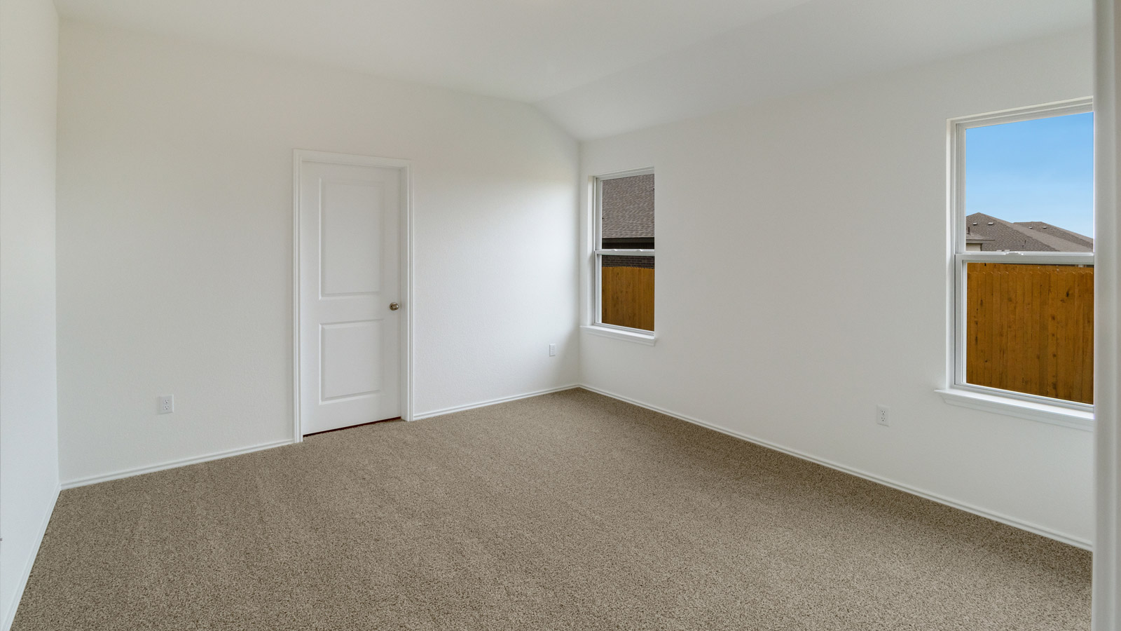Spacious primary bedroom with beige carpet, white walls and two windows