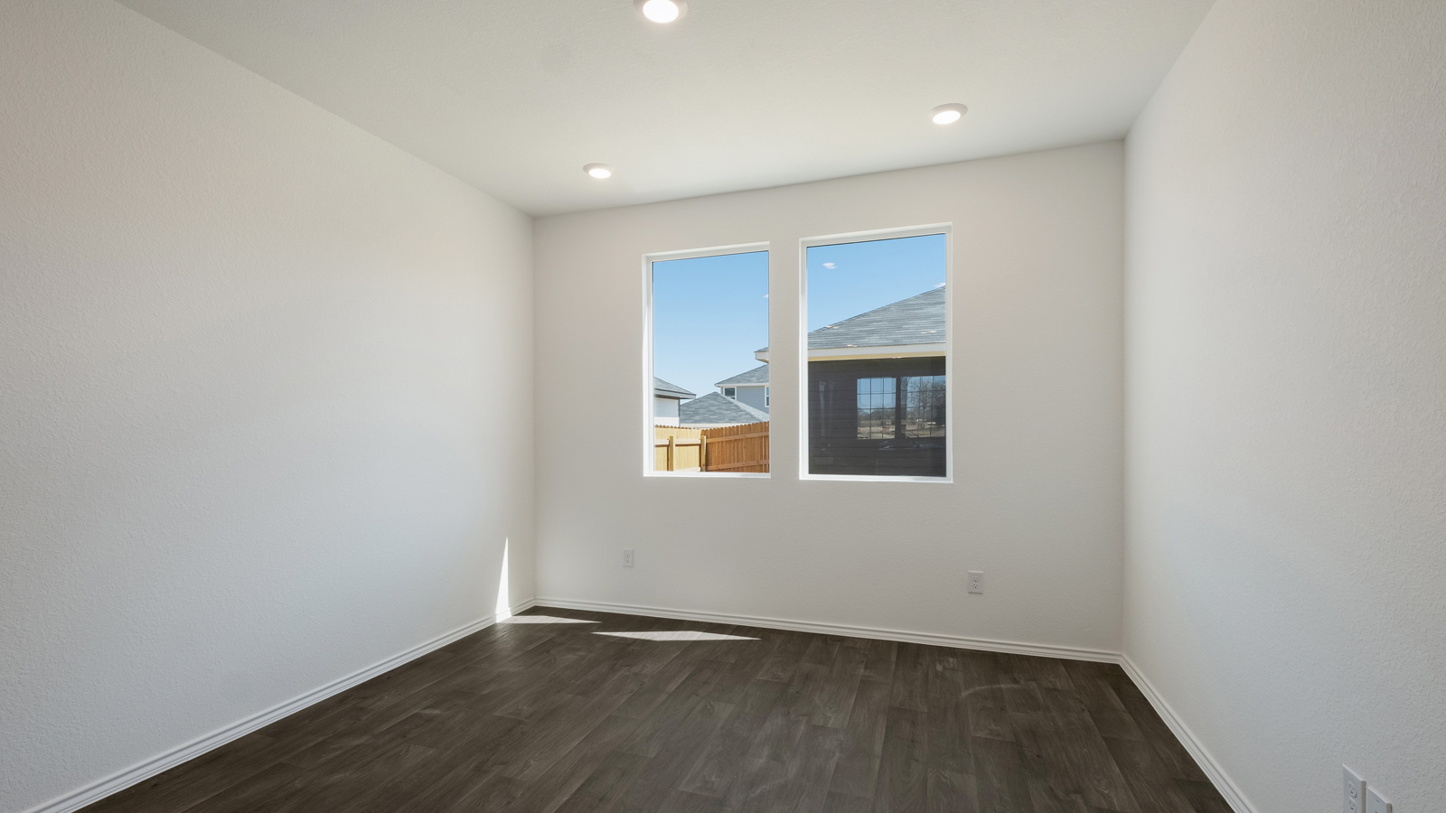 Spacious living room with brown flooring, white walls and windows