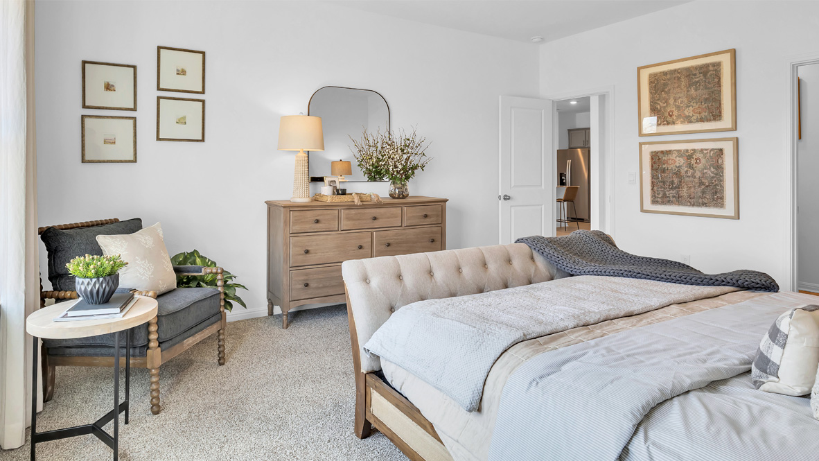 Cozy bedroom with a wooden dresser, a large mirror, and a table lamp. A plush bed is adorned with soft blankets. Neutral tones create a calm ambiance.