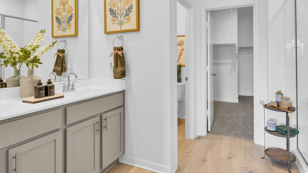 Bright bathroom with a dual-sink vanity and decorative wooden cabinet. Floral prints hang above, enhancing the serene, elegant atmosphere.