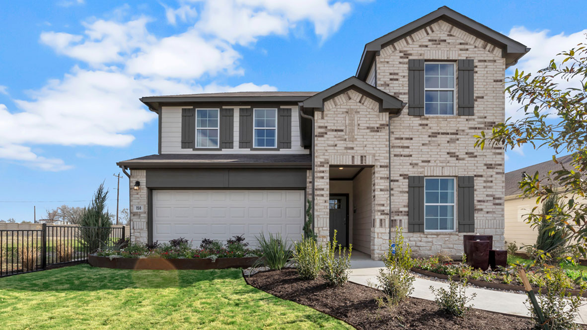 Modern two-story house with light brick exterior, dark shutters, and a two-car garage. Front yard features manicured lawn and shrubs under a clear blue sky.