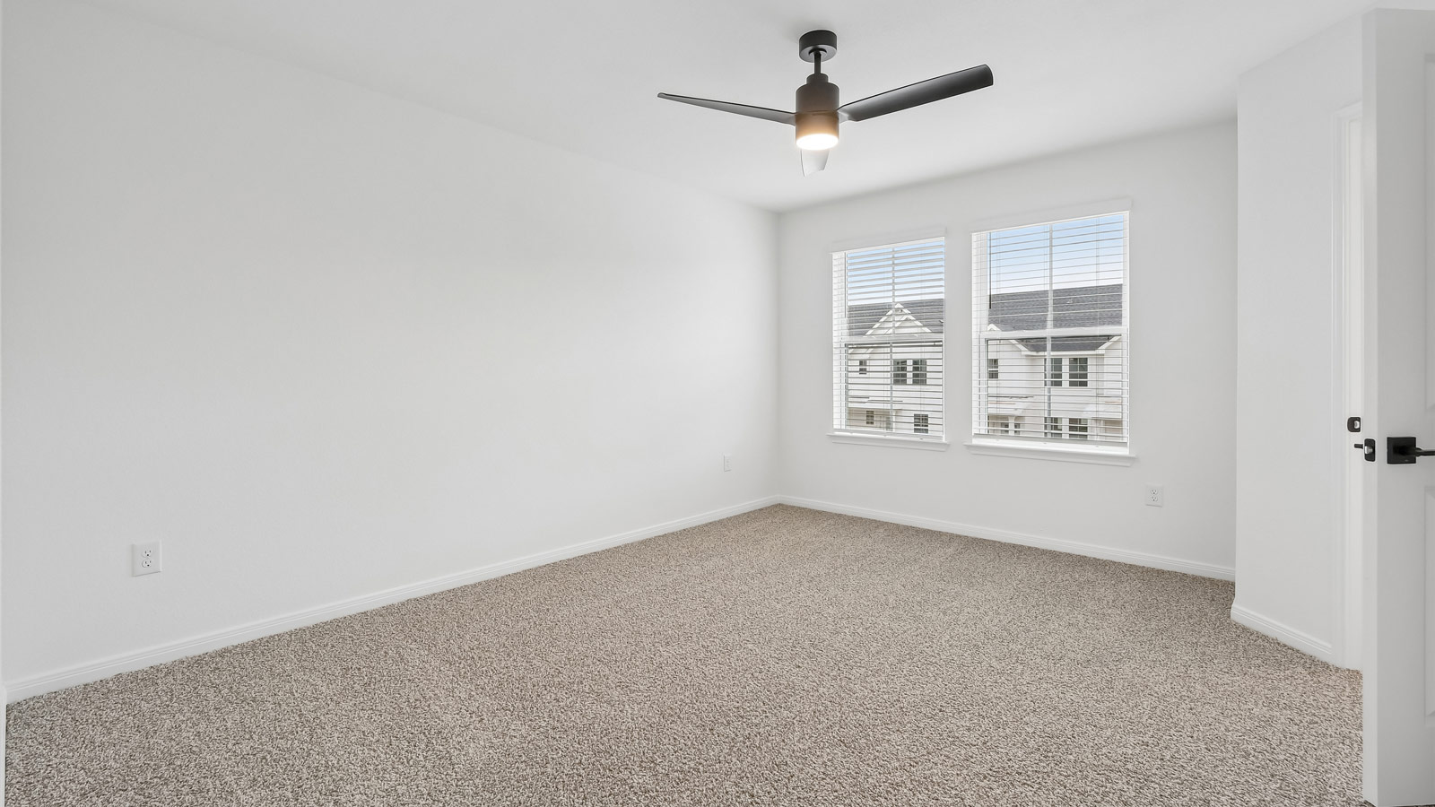 Primary bedroom with carpeted flooring, ceiling fan, and windows.