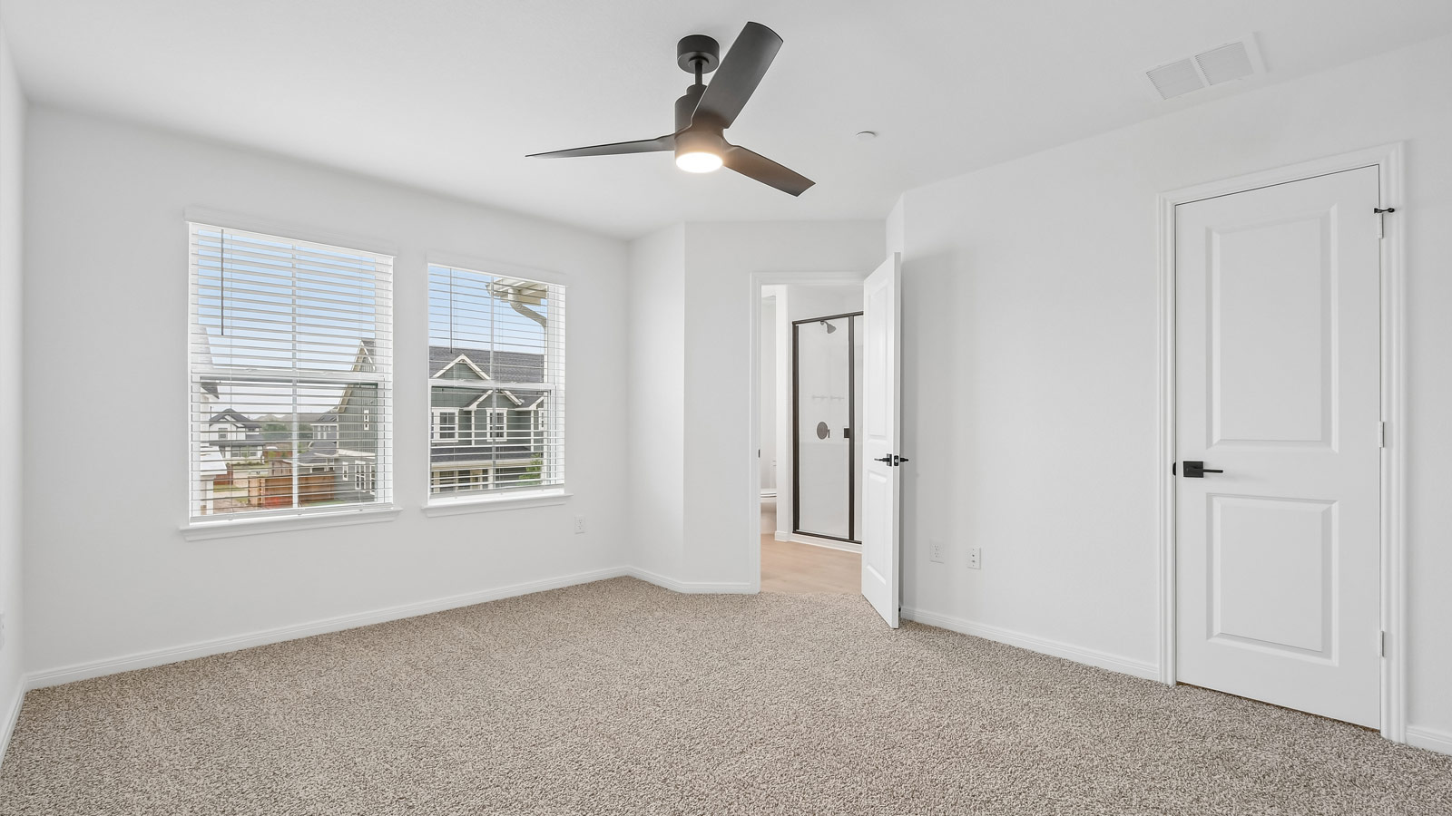 Primary bedroom with carpeted flooring, ceiling fan, and windows.