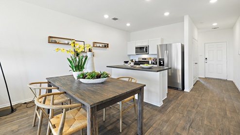 View of dining room with a wooden table and 6 wooden chairs overlooking the kitchen