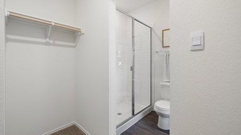 bathroom featuring a walk in tiled shower, a toilet next to it and a hanging rod