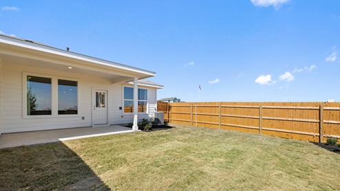 rear exterior view of this home featuring a covered patio, green grass and a wooden fence