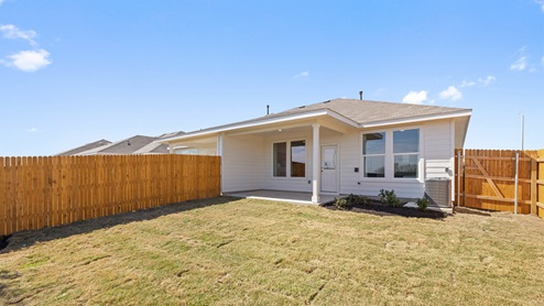 rear exterior view of this home featuring a covered patio, green grass and a wooden fence