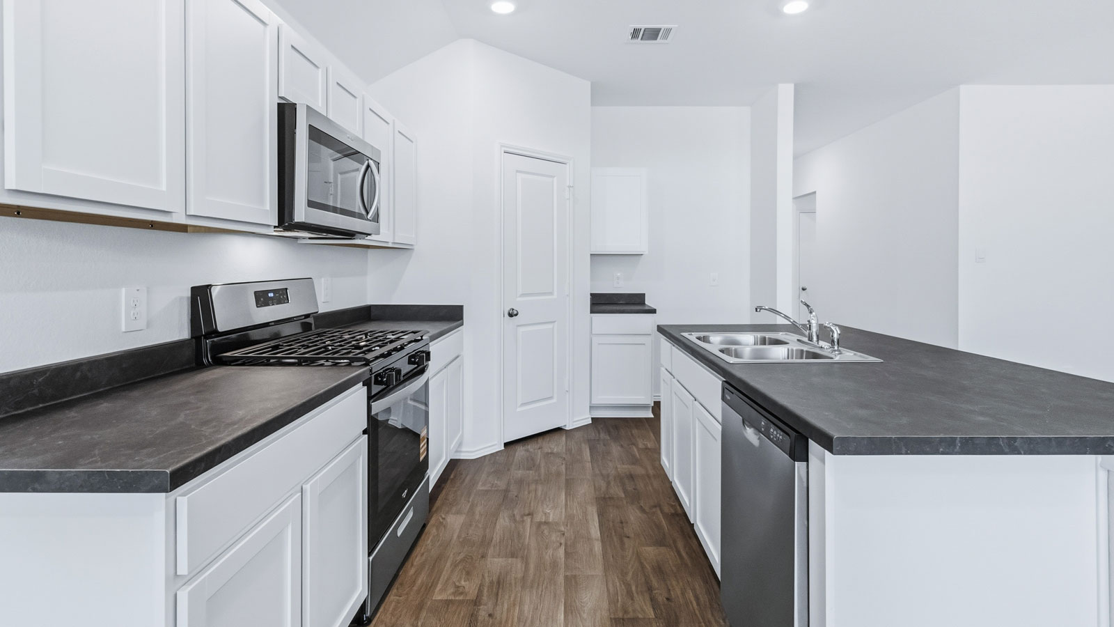 Side view of kitchen to pantry, cabinets, near front door and living areas, appliance suite included