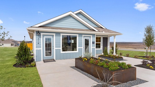 Front exterior of a 1 story model home with light blue siding and beautiful landscaping