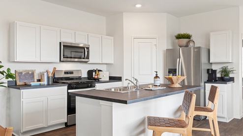 spacious kitchen with white cabinetry, stainless steel appliances, large kitchen island, and 2 large windows bringing in natural light