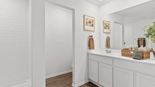 Modern bathroom featuring rich brown floors, white cabinetry and a large mirror