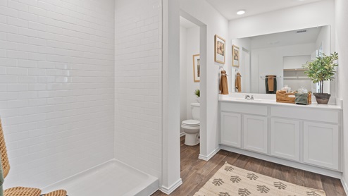 Modern bathroom featuring rich brown floors, white cabinetry and a large mirror