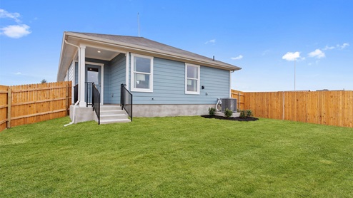 Rear exterior view of the one story model home with light blue siding. It features a fence and beautiful grass